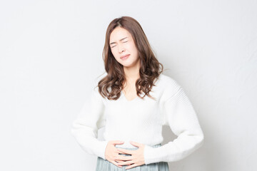 白い壁の前に立って、お腹に手を当てる若い女性